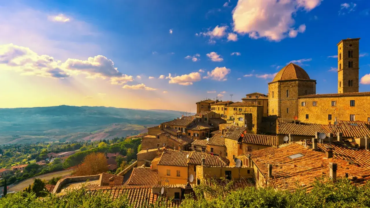 Un borgo toscano al tramonto, con tetti in cotto e un campanile svettante. Curiosità sulla Toscana: questo paesaggio evoca storie antiche.