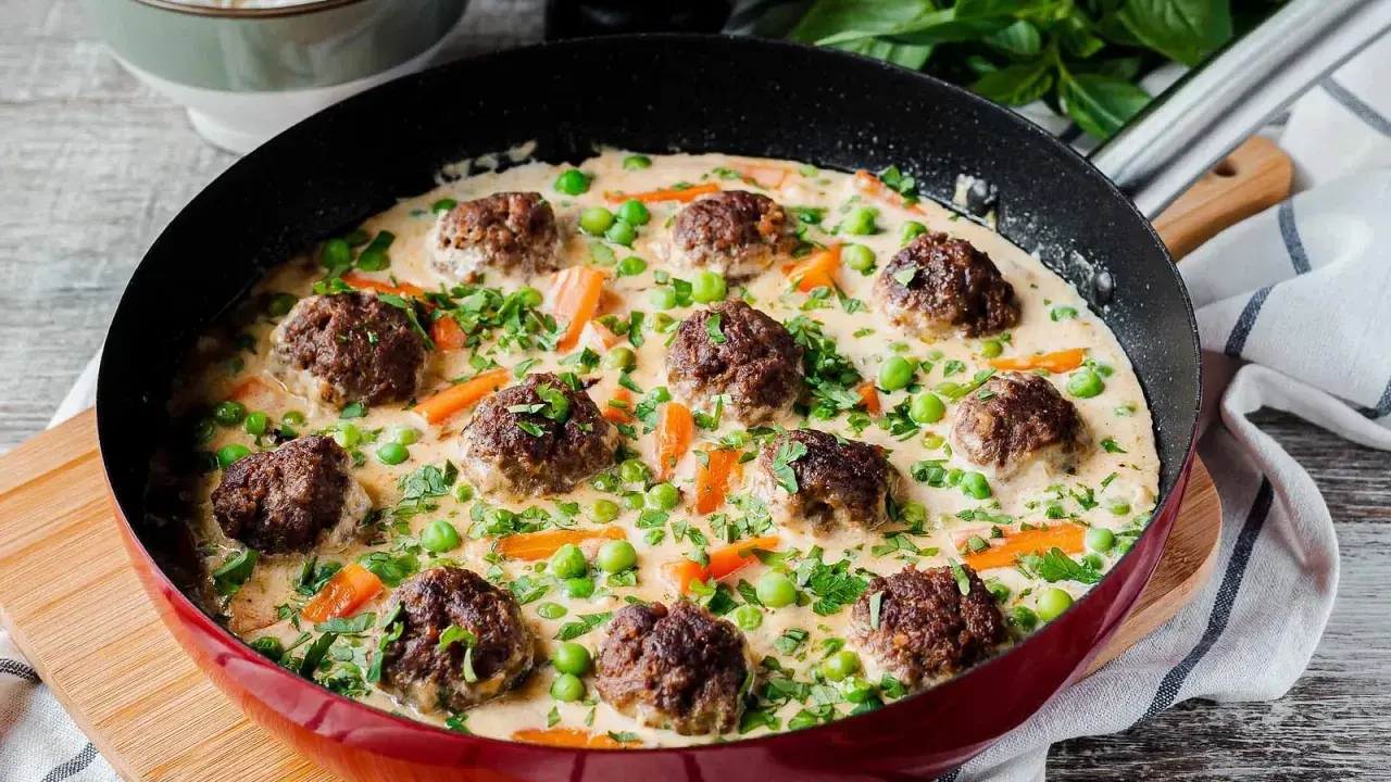 Herzhafte Fleischbällchen in cremiger Sauce mit Erbsen und Karotten, ein köstliches Wikingertopf Rezept, serviert in einer roten Pfanne.