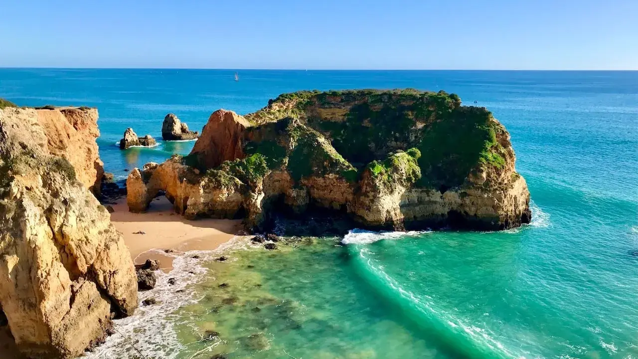 Traumhafte Felsformationen und türkisfarbenes Wasser am Praia de Alvor. Eine kleine Bucht mit Sand und grünen Klippen.