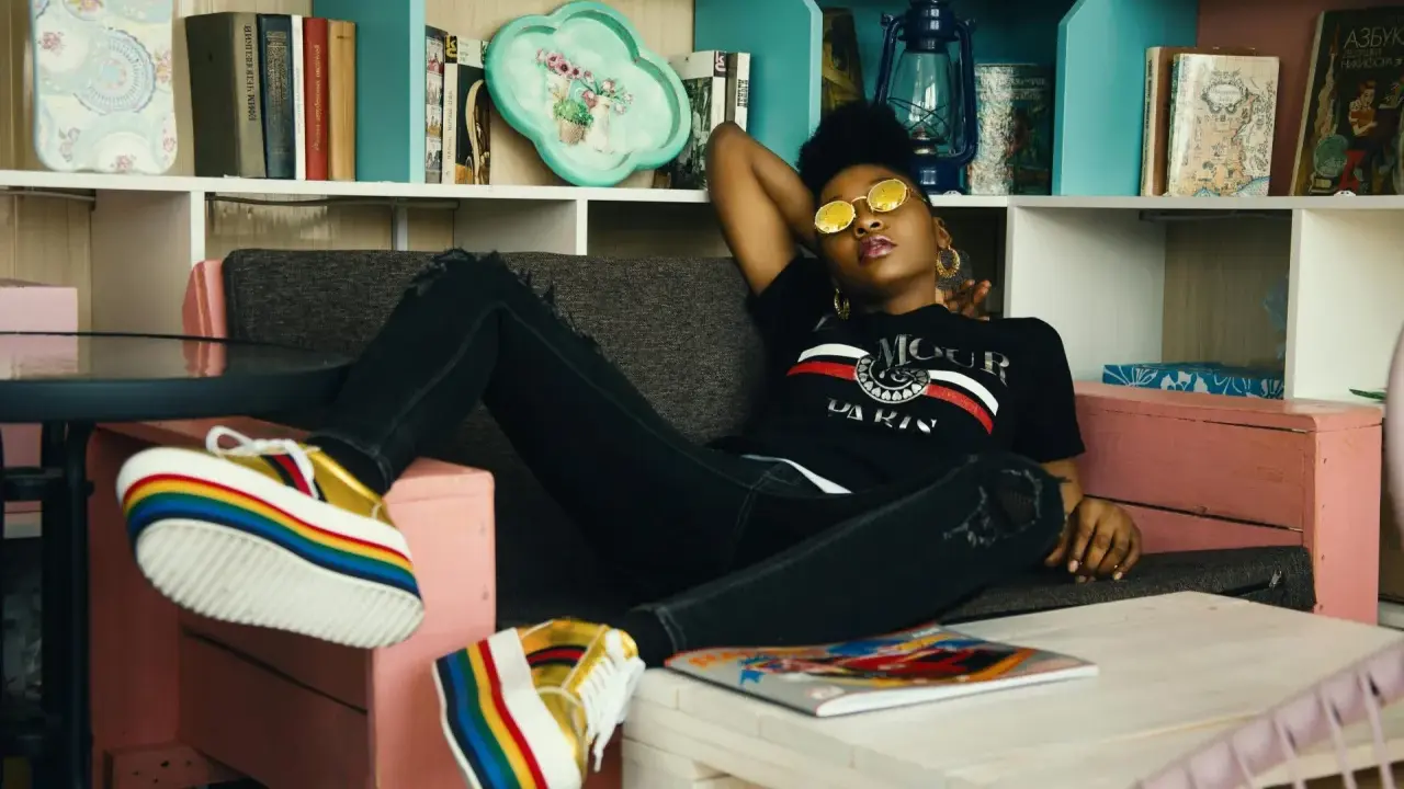 Une jeune femme aux lunettes rondes dorées se détend sur un canapé, ses chaussures arc-en-ciel colorées bien en évidence. Elle incarne le parfait "chill traduction".