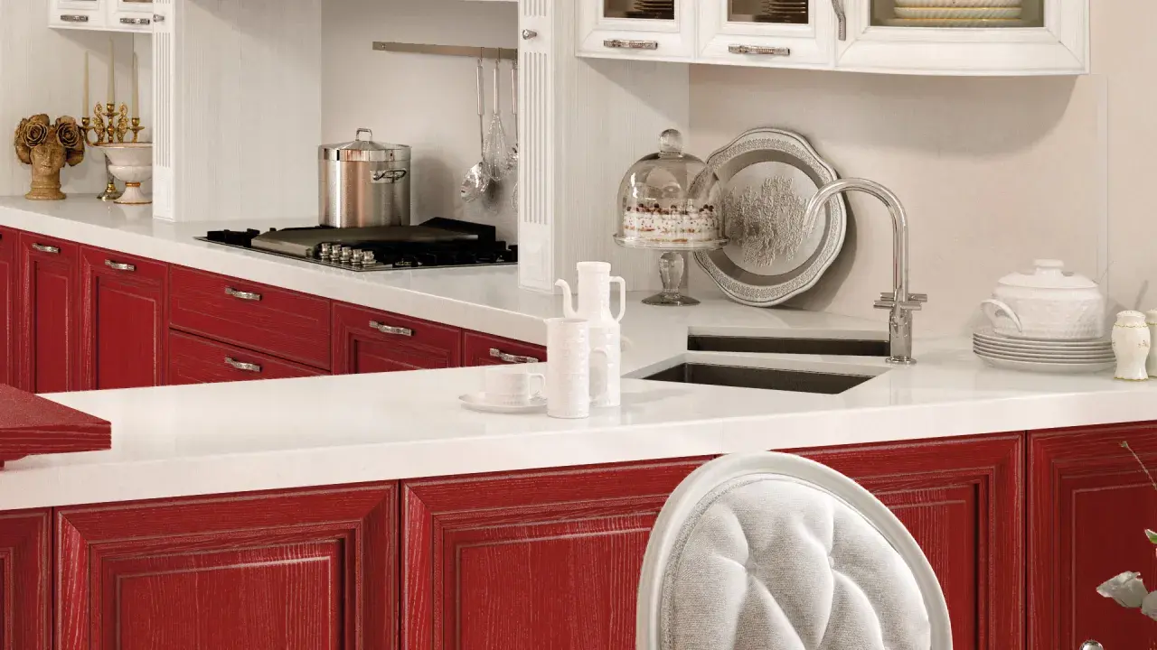 Cucina con ante rosse, piano bianco, pentola sul fornello, torta sotto campana di vetro. Okite cos'è? Un piano di lavoro resistente e bello.