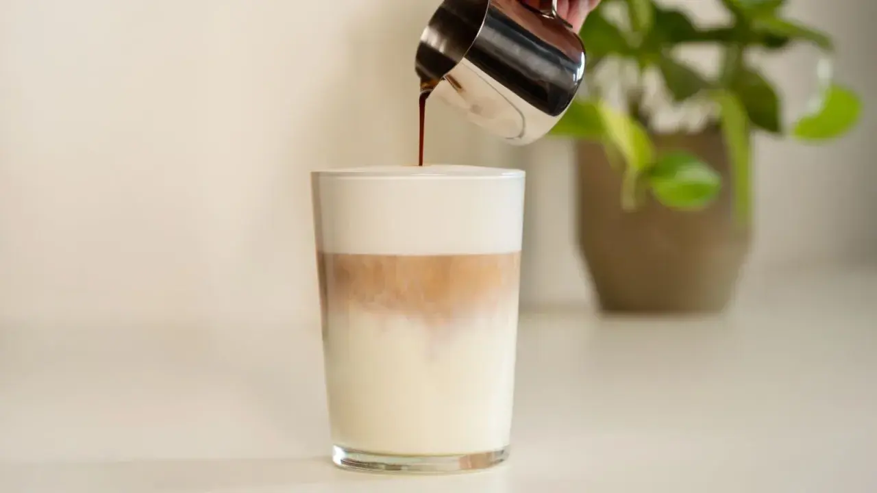 Espresso wird in ein Glas mit Milch und Milchschaum gegossen. Ein perfektes Latte Macchiato Rezept.