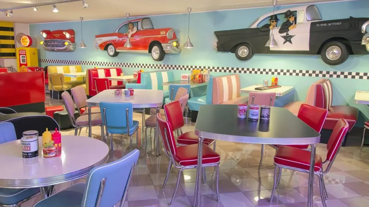 Interni di un diner in **stile americano** con sedili color pastello, tavoli cromati e decorazioni a tema auto d'epoca.