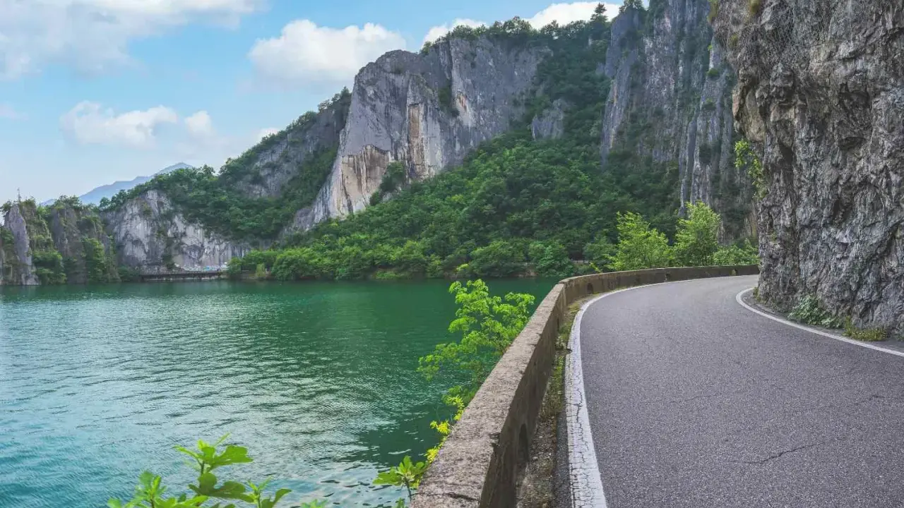Strada panoramica lungo un lago verde smeraldo, con imponenti pareti rocciose e vegetazione lussureggiante. Un percorso suggestivo per raggiungere la baia di Bogn.