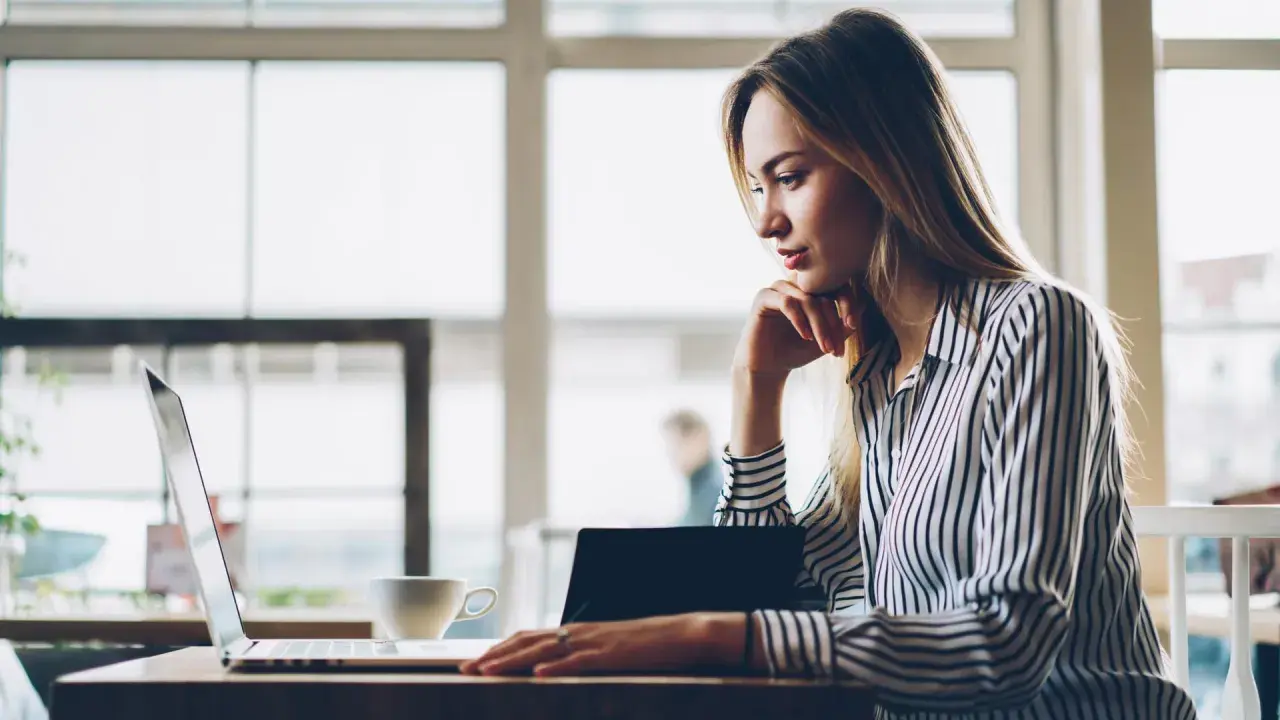 Donna pensa a come fare un webinar, seduta al laptop con una tazza di caffè.