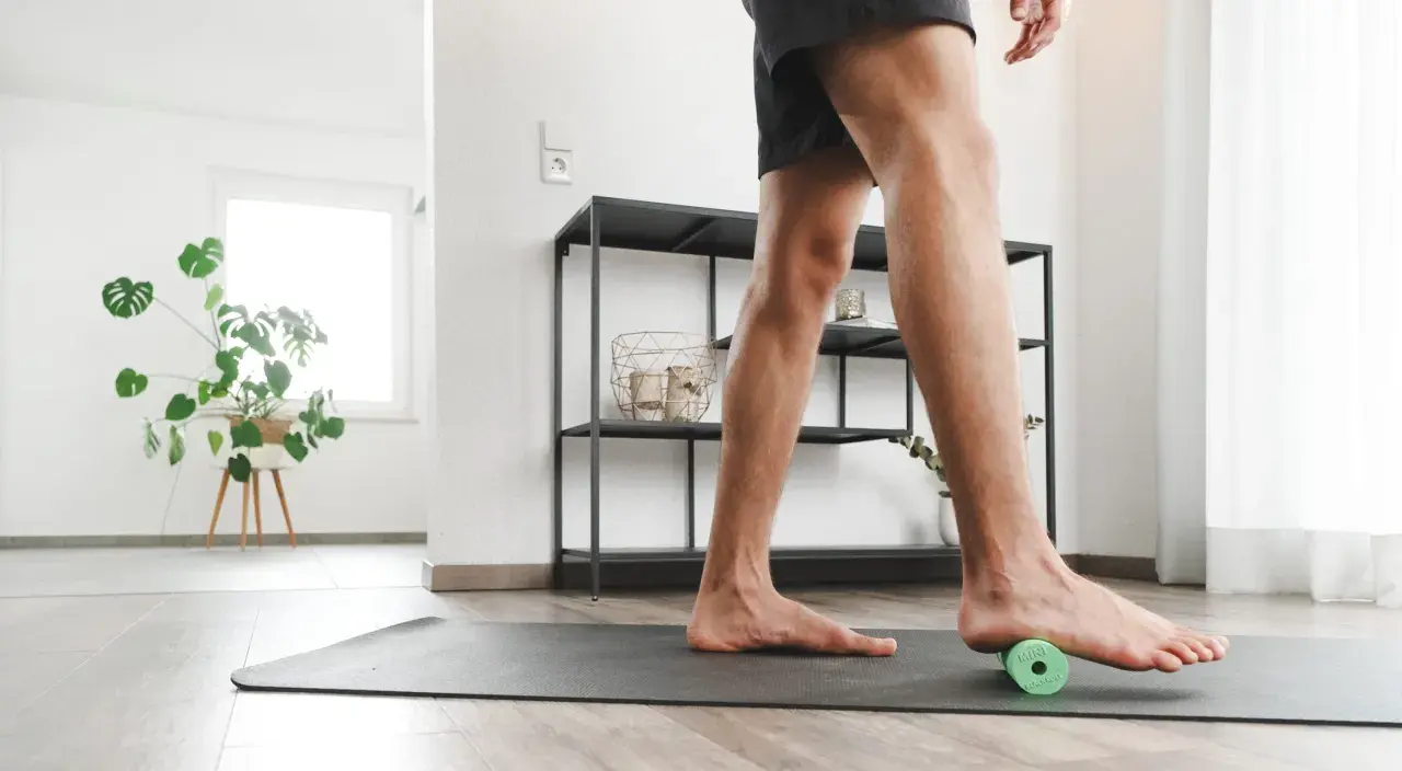 Mann rollt mit einem kleinen grünen Ball unter dem Fuß, um Plantarfasziitis-Hausmittel anzuwenden.