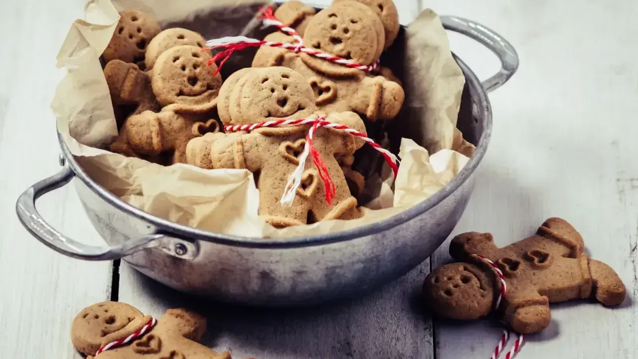 Un cuenco lleno de galletas de jengibre con caritas sonrientes y corazones, atadas con hilo rojo y blanco.