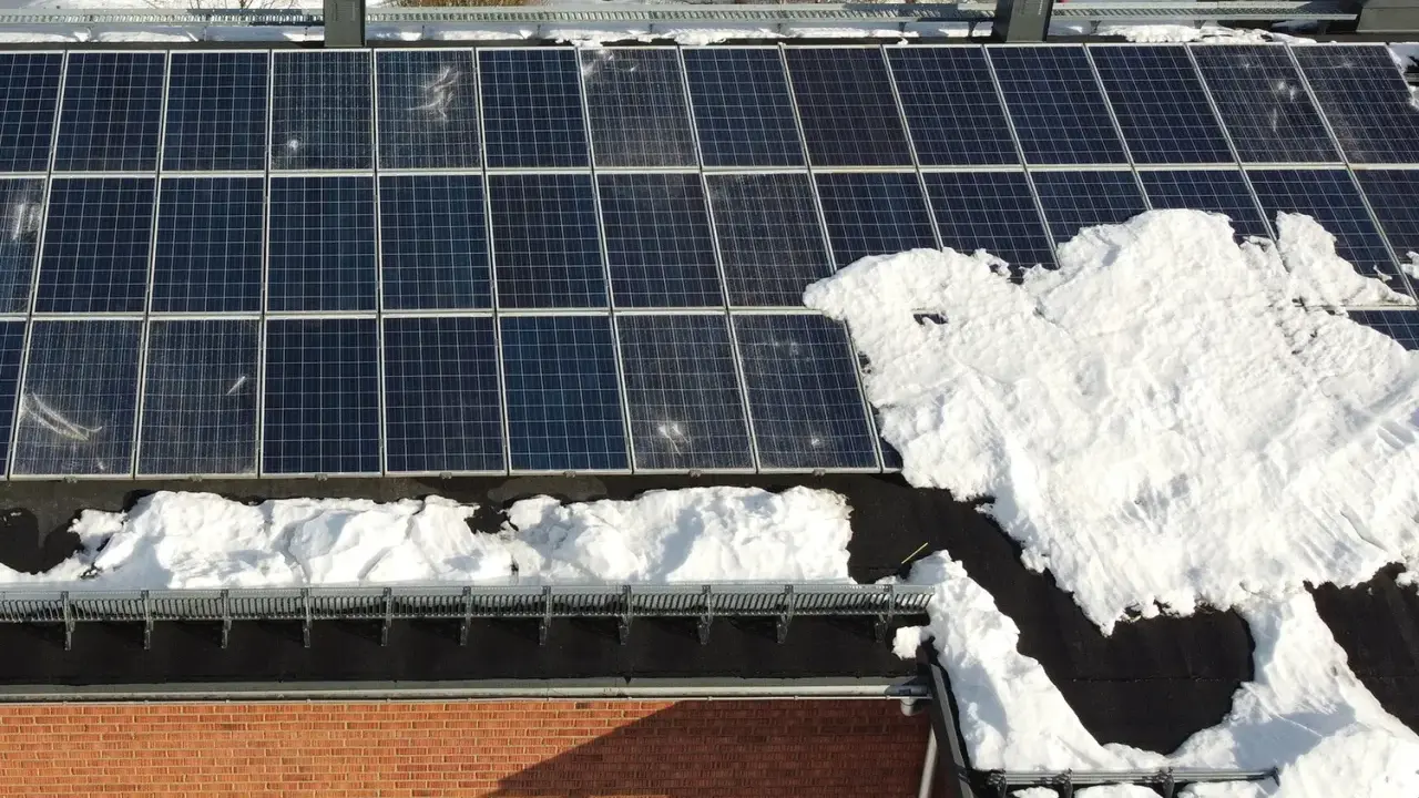 Snö täcker delar av solpanelerna på ett tak. Snart är det dags att skotta solpaneler för att fånga solens energi igen.