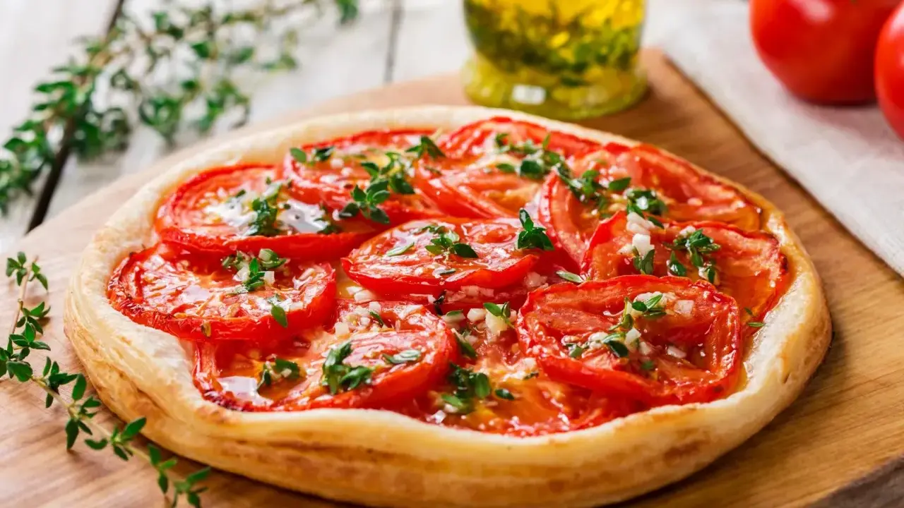 Tarte aux tomates cerises, garnie d'herbes fraîches et d'ail, prête à être dégustée.