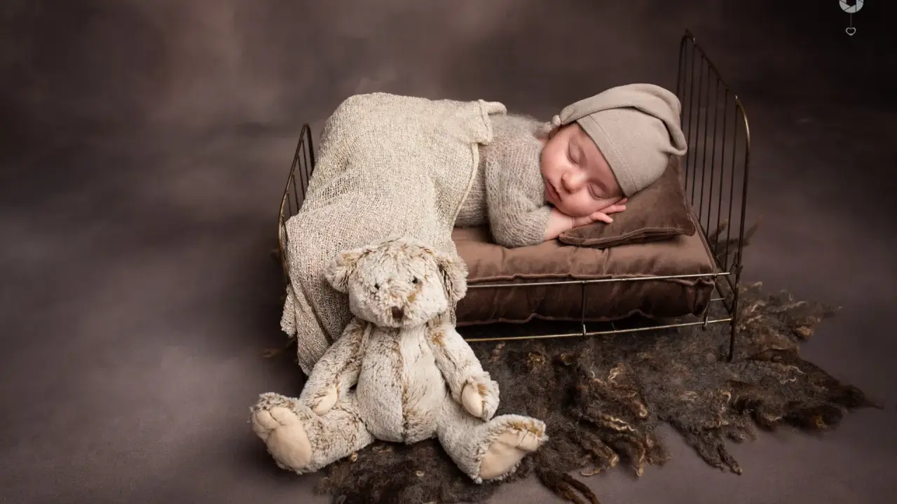 Dolce bimbo appena nato dorme sereno in una culla con un orsacchiotto. Foto bimbi appena nati.
