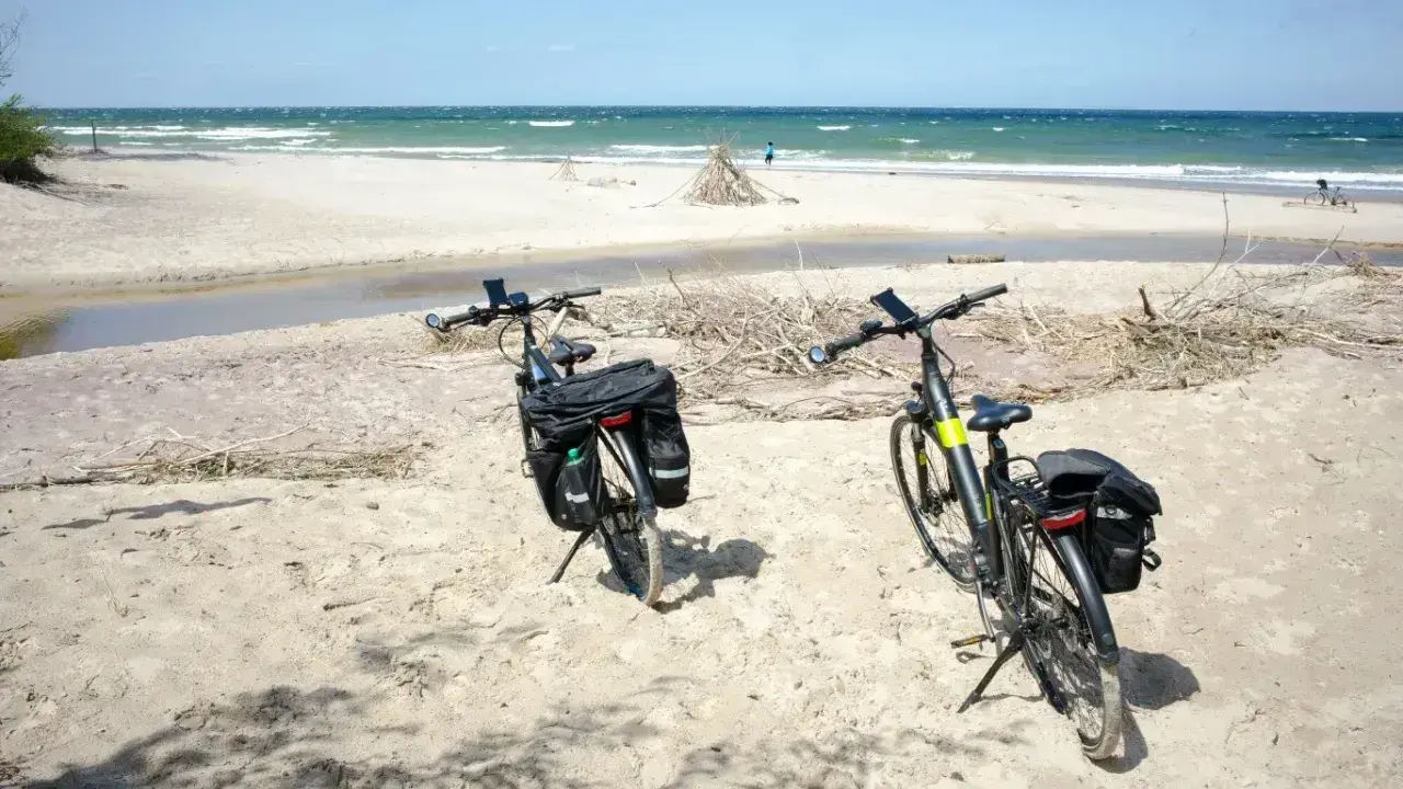 Dwa rowery z sakwami na piaszczystej plaży, gotowe na odkrywanie płaskich tras rowerowych nad morzem.