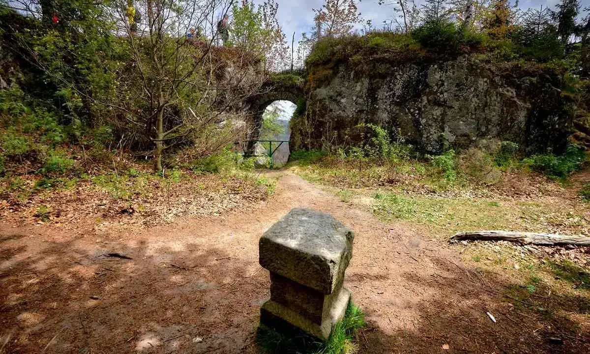Kamienny postument przed łukiem w fort karola. Ścieżka prowadzi przez zarośla do zabytkowej budowli.