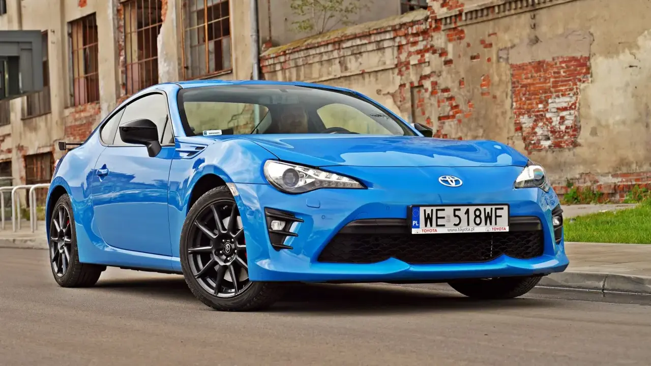 Błękitna Toyota GT86, znana też jako Toyota BRZ, zaparkowana przed zniszczonym budynkiem.