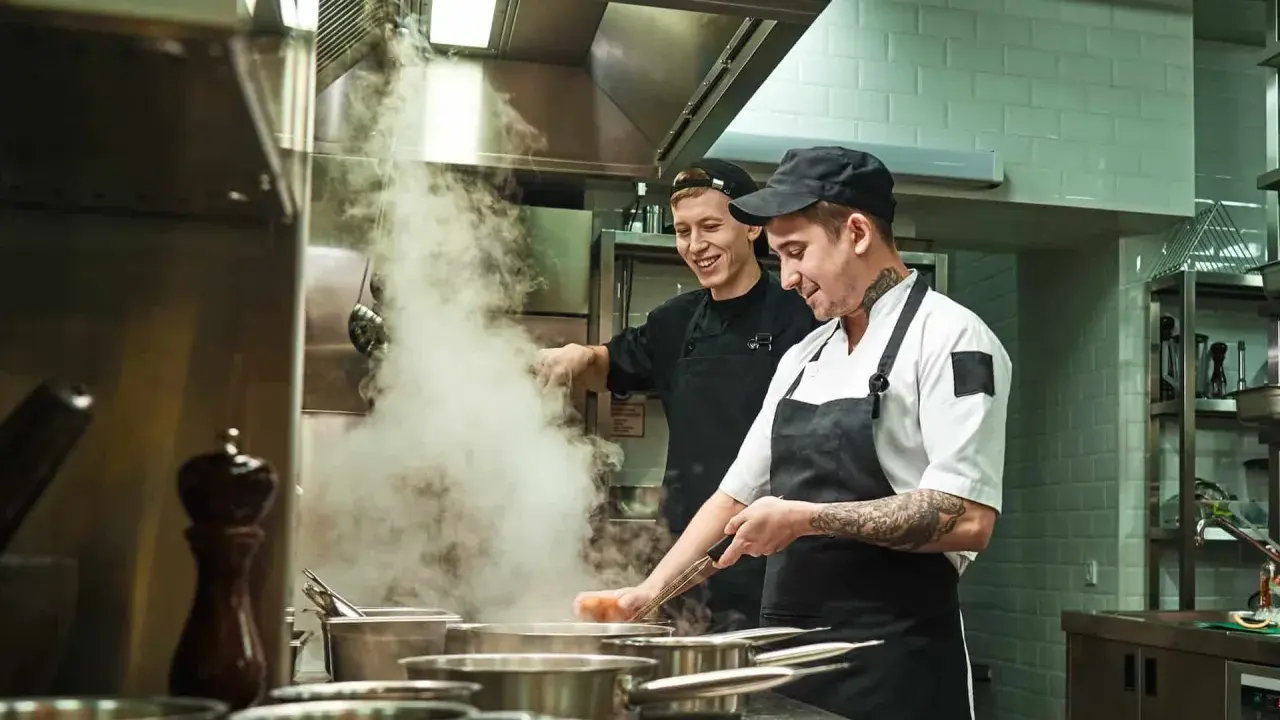 Deux chefs travaillent dans une cuisine de restaurant, respectant la norme de qualité. Vapeur s'échappant des casseroles.