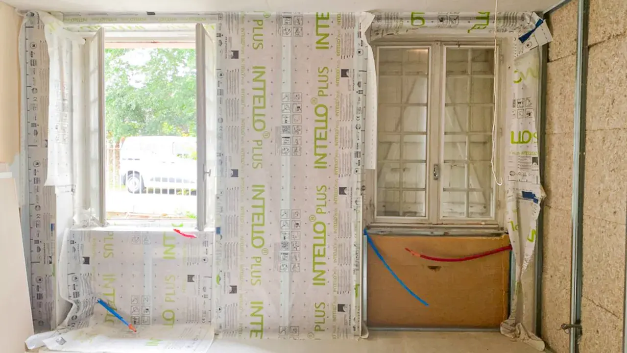 Pose de pare-vapeur pour comment isoler un mur intérieur. Fenêtres, tuyaux et ossature métallique visibles.