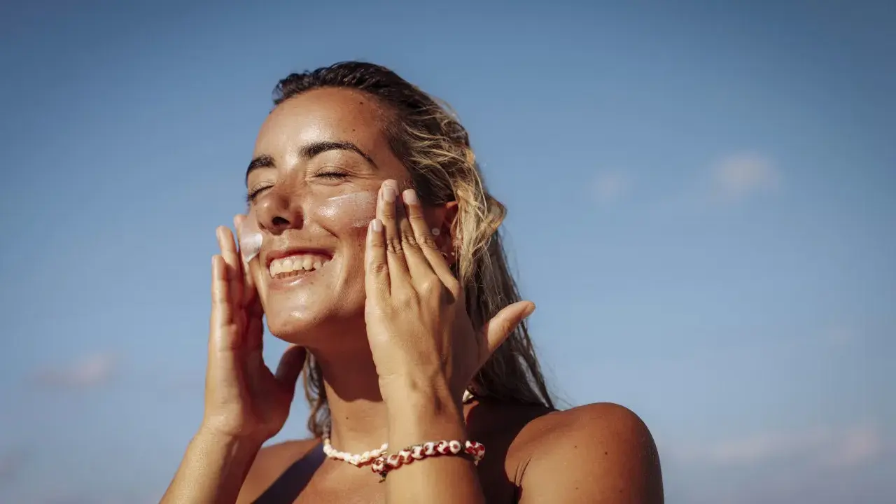 Donna sorridente applica crema solare per proteggere la pelle da macchie e tumore.