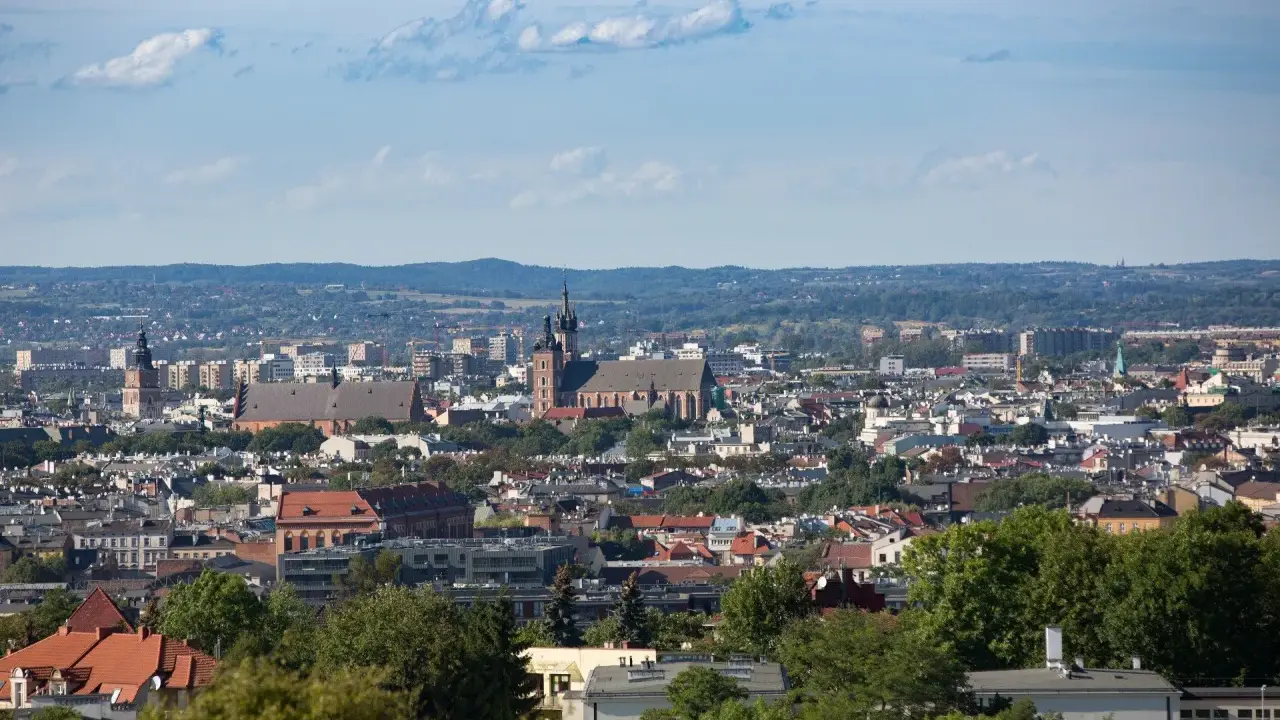 Widok na Kraków z punktu widokowego. W oddali widać kościół Mariacki i Wawel, a bliżej zabudowania miejskie i zieleń.