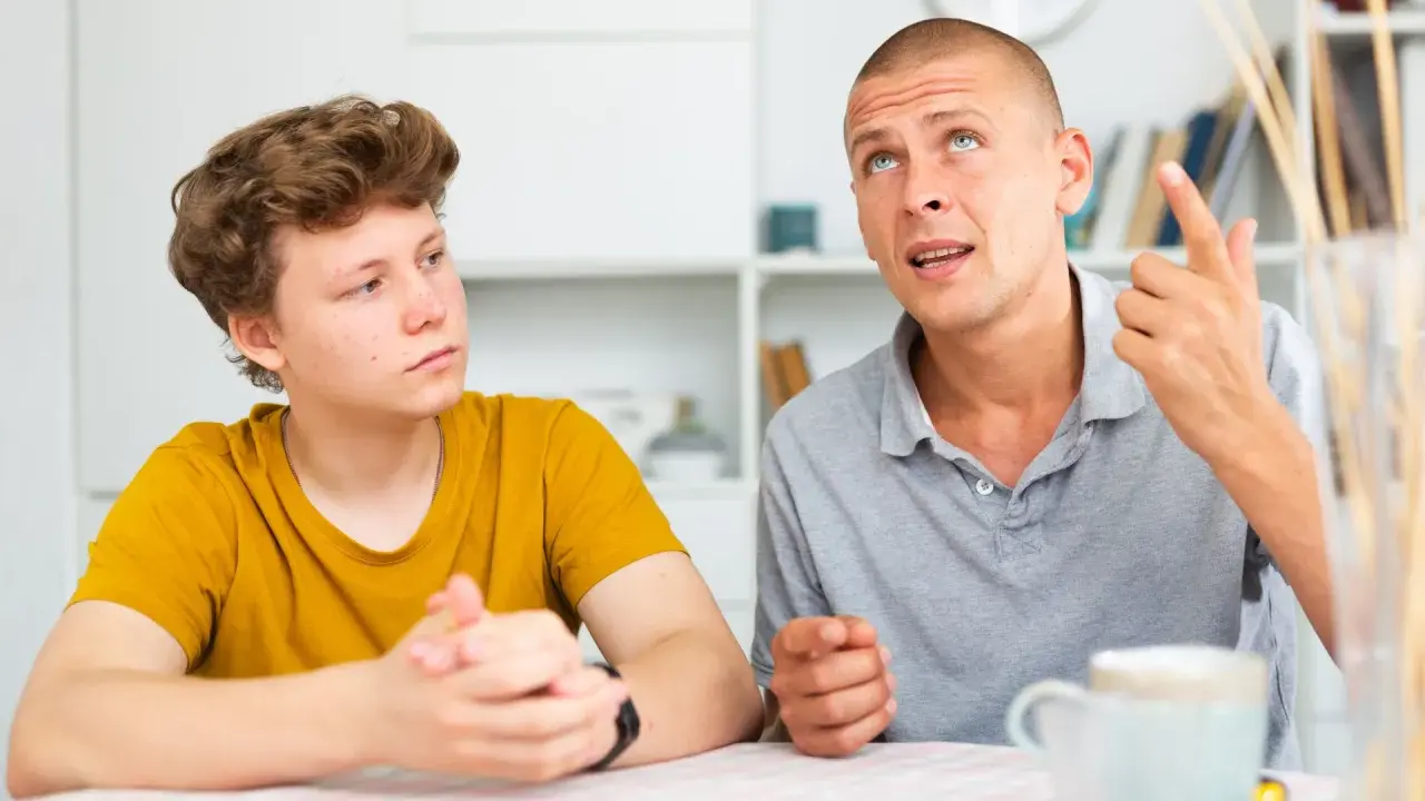 Ojciec tłumaczy synowi, jak rozmawiać z nastolatkiem, używając gestów. Chłopak słucha uważnie.