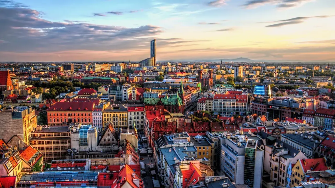 Widok na Wrocław, największe miasto zachodniej Polski, z dominującym wieżowcem Sky Tower. Słońce zachodzi nad kolorowymi dachami kamienic.