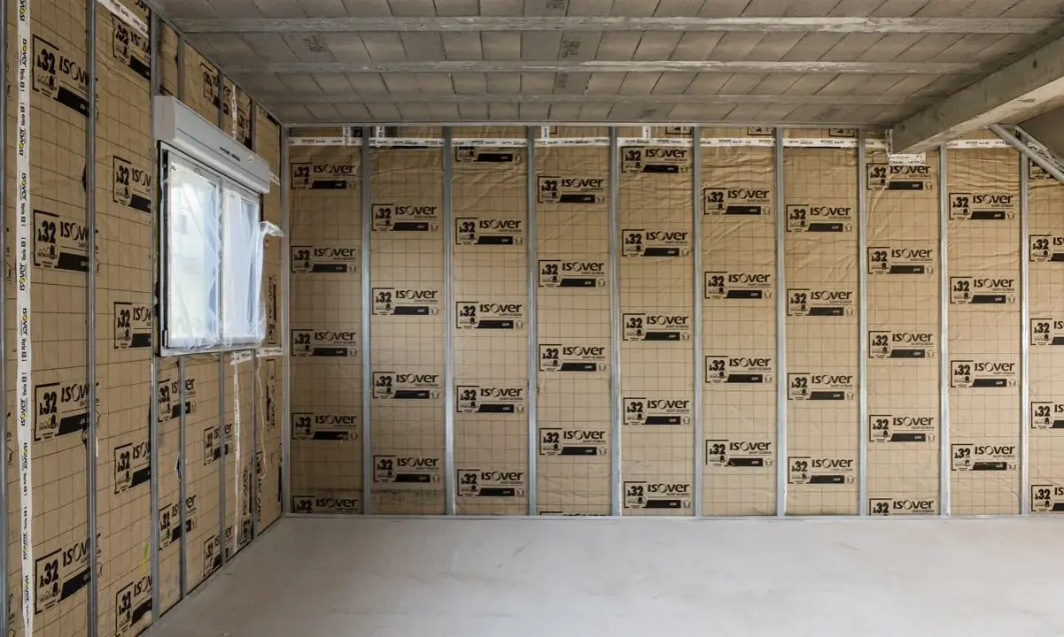 Le chantier progresse, on commence à isoler un mur avec des panneaux Isover. Une fenêtre est visible sur la gauche.