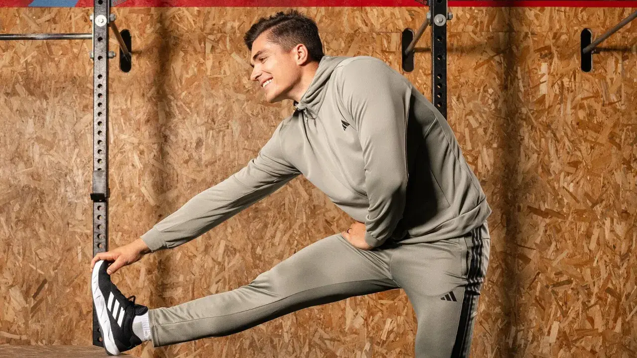 Ein Mann in Trainingskleidung macht dynamisches Dehnen vor einer Holzwand.
