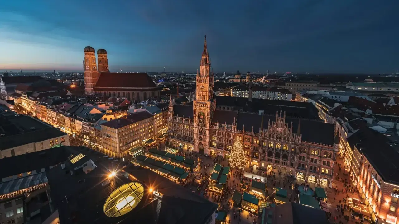 Nocny jarmark bożonarodzeniowy w Monachium. Rynek z oświetlonymi straganami i choinką, w tle Frauenkirche i Nowy Ratusz.