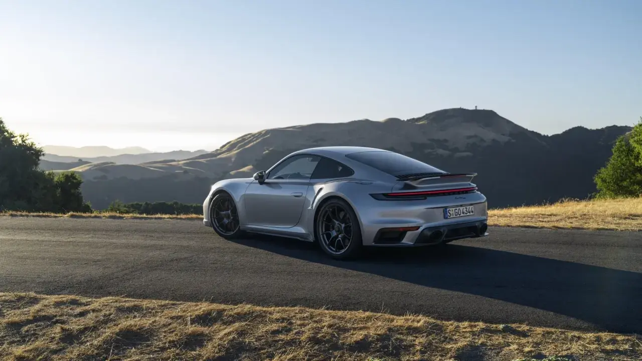 Silberner Porsche 911 Turbo S, ein Sondermodell 2023, parkt auf einer Bergstraße mit sanften Hügeln im Hintergrund.