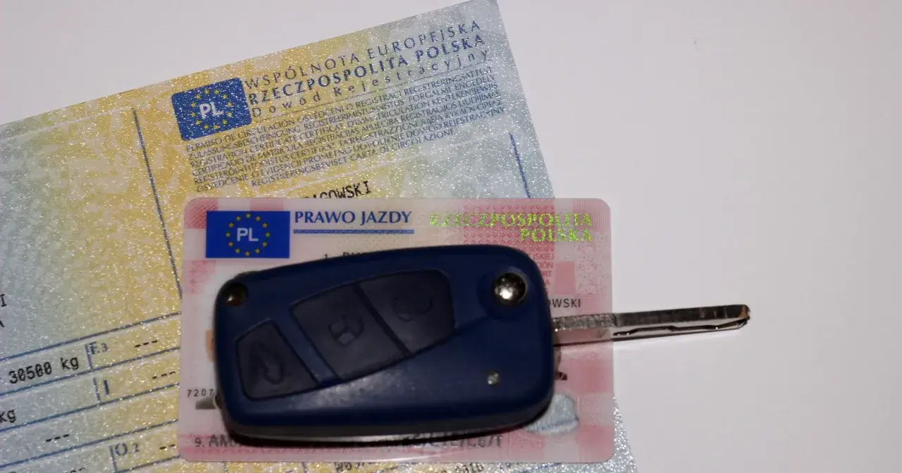 Kluczyk samochodowy leży na dowodzie rejestracyjnym i prawie jazdy. To komplet dokumentów do prowadzenia pojazdu.