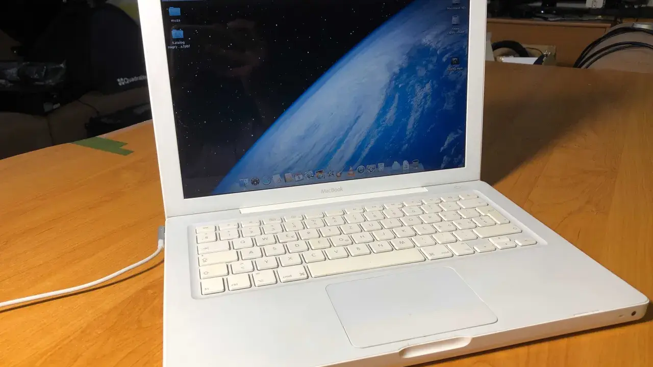 Biały, pierwszy MacBook z widokiem Ziemi na ekranie, stoi na drewnianym stole.