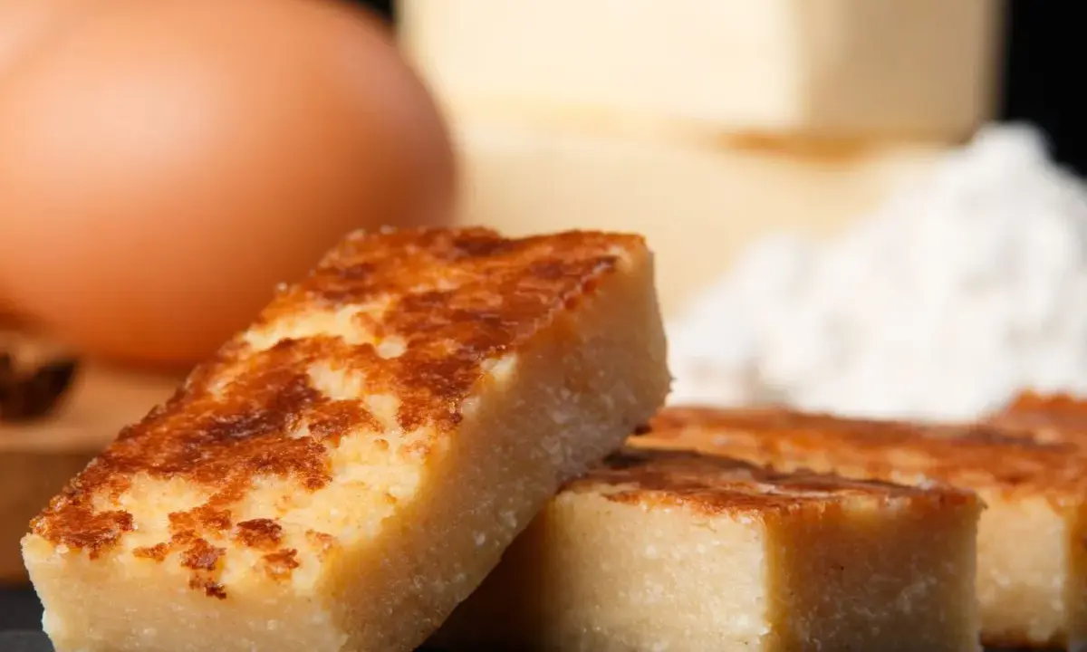 Porciones doradas de quesada, con huevos y harina al fondo. Ingredientes para una deliciosa receta quesada.