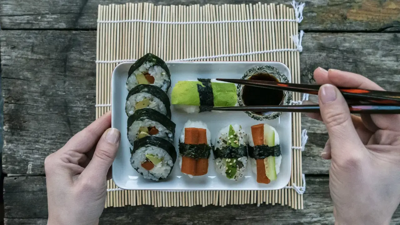 En bricka med olika sorters sushi, perfekt för ett enkelt sushi recept. En hand håller ätpinnar redo att plocka upp en bit.