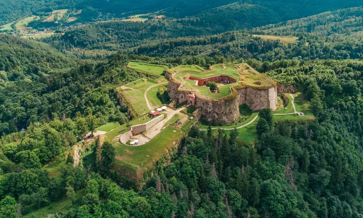 Forteca na zielonym wzgórzu, niczym srebrna góra, otoczona lasem.