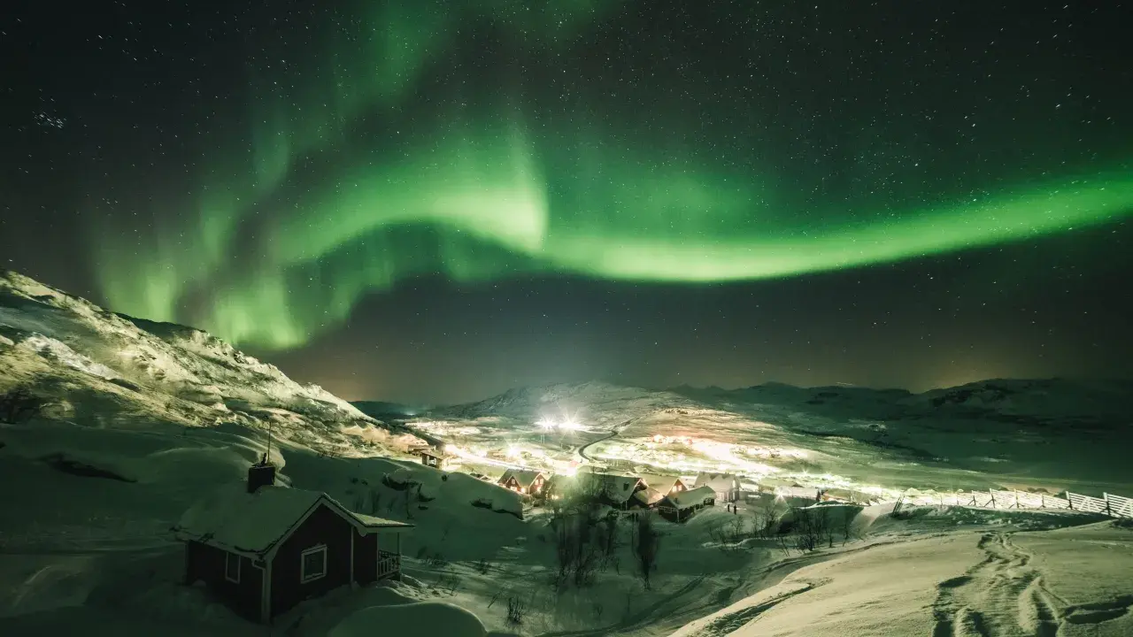 En snötäckt by i Sverige badar i det magiska skenet från norrskenet.