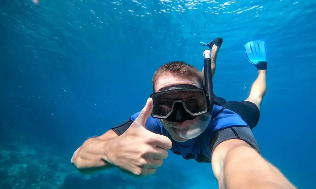 En man snorklar och ger tummen upp i det klara vattnet vid Nerja strand.