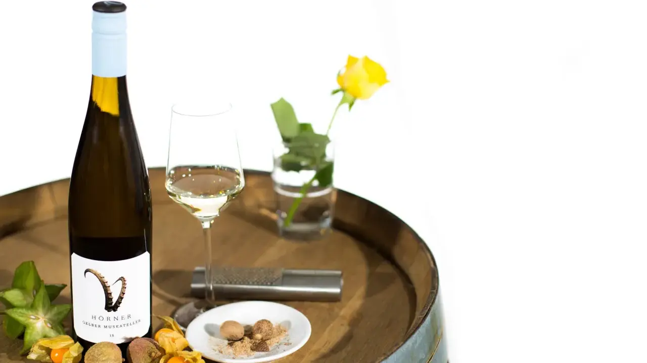 Flasche Gelber Muskateller Wein, Glas, Sternfrucht, Physalis, Litschi und Muskatnuss auf einem Holzfass.