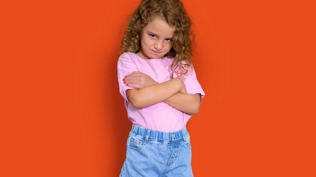 Niña con rizos, brazos cruzados y expresión de enfado. Podría representar la **depresión infantil** o simplemente un mal humor pasajero.