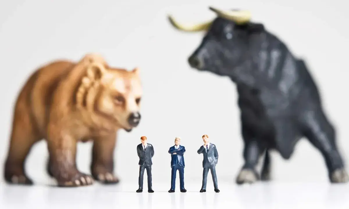 Miniature businessmen stand between a bear and a bull, symbolizing market volatility and the quest for art investment returns.