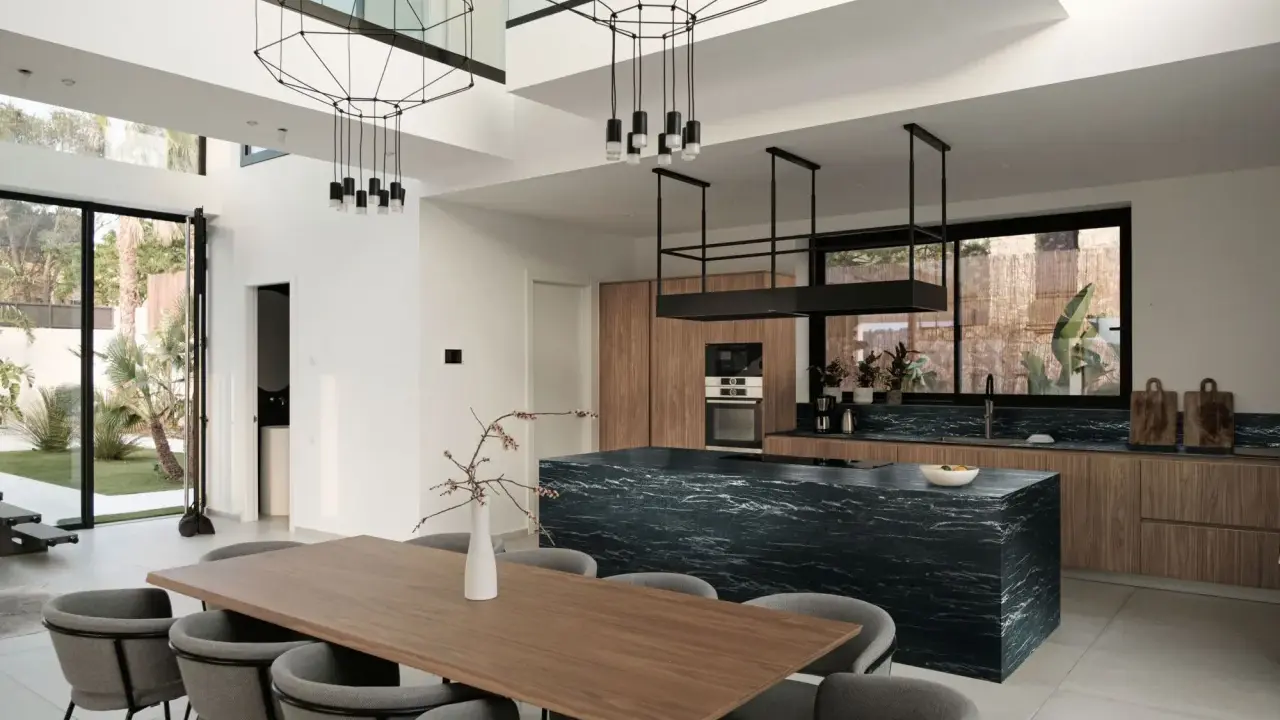 Nowoczesny salon z kuchnią otwartą: drewniane meble, czarna wyspa kuchenna, designerskie lampy i duży stół jadalniany.
