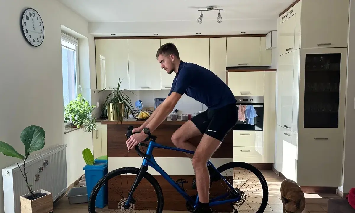 Mężczyzna w pozycji na rowerze gravel w kuchni, obok niego pies.