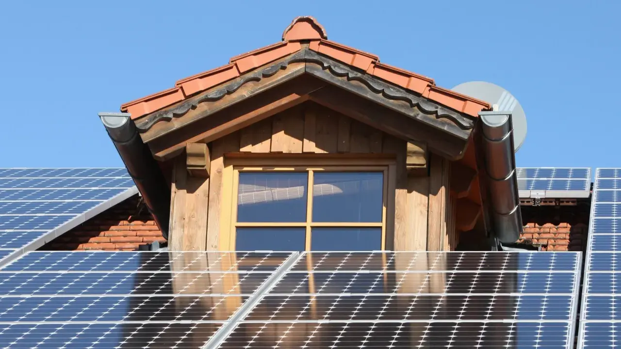 Dach mit Solarmodulen, die erneuerbare Energie von der Sonne einfangen. Ein Fenster und ein Dachüberstand aus Holz sind sichtbar.