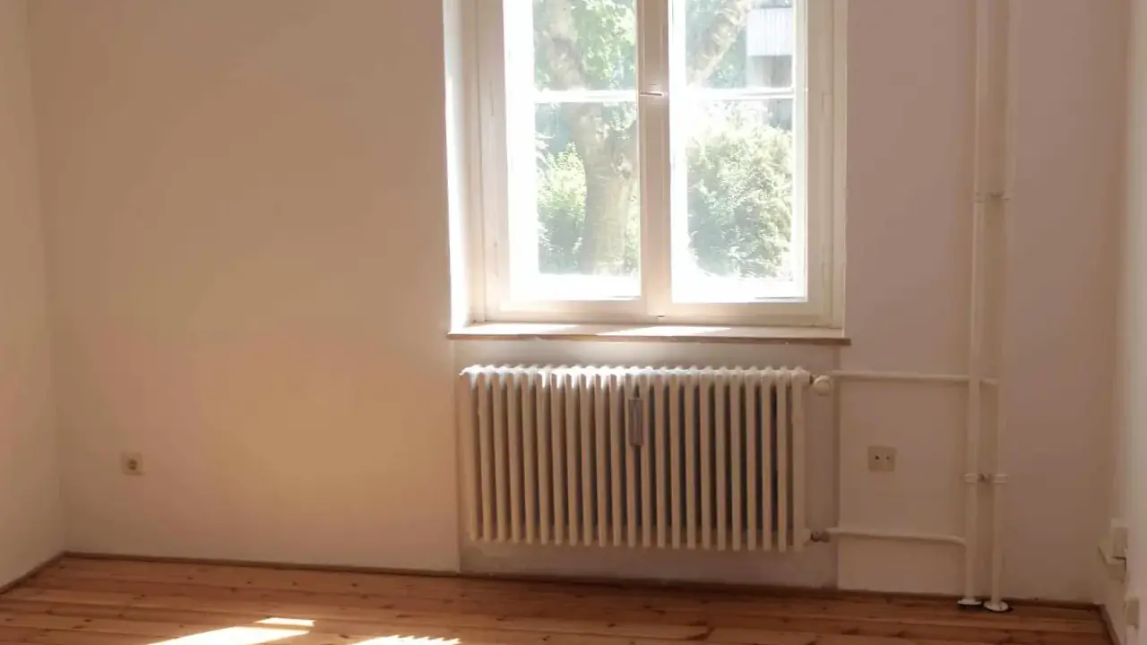 Jasne, oto opis:

Drewniana podłoga, biały grzejnik i parapet nad nim. Za oknem widać drzewa.