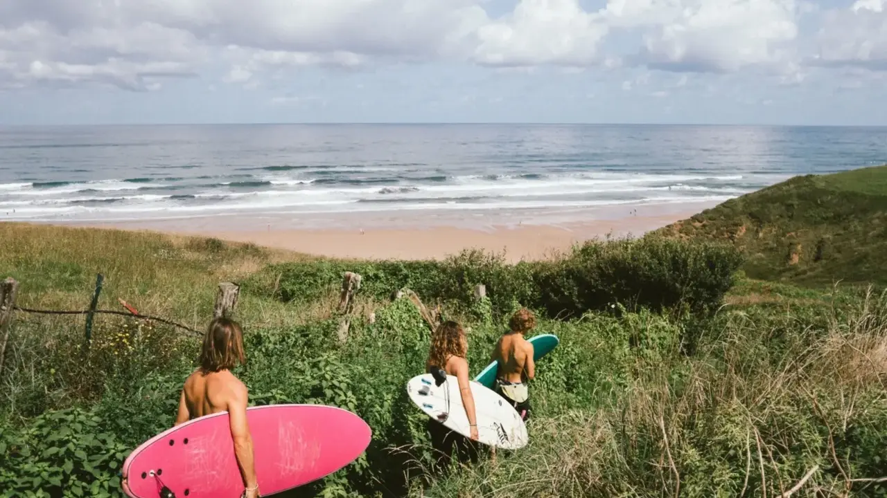 Drei Freunde mit Surfbrettern auf dem Weg zum Strand in Spanien. Die Wellen laden zum Surfen ein.
