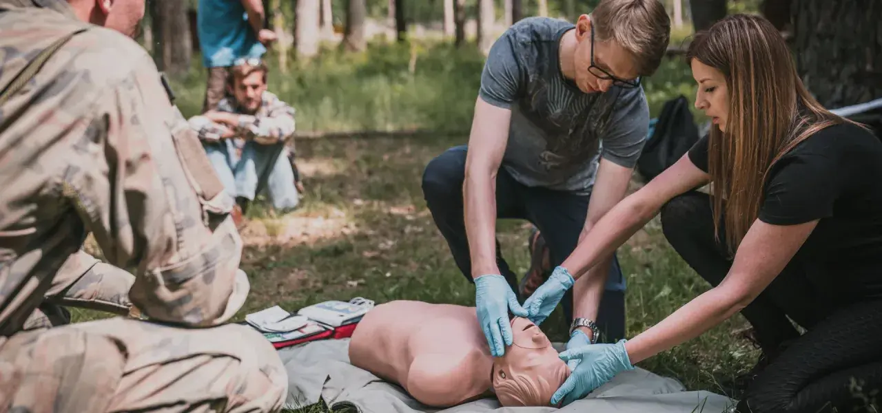 Uczestnicy kursu przetrwania ćwiczą resuscytację na fantomie w lesie.