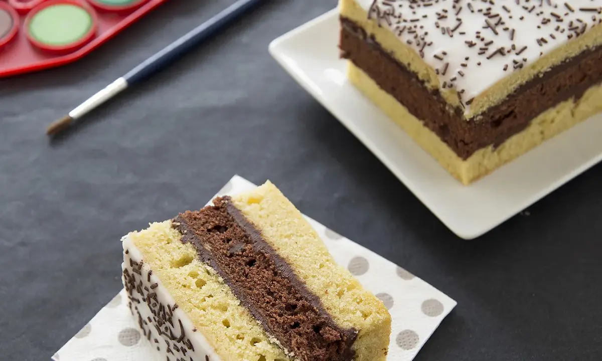Gâteau napolitain, le meilleur pâtissier. Une part sur une serviette, une autre entière sur une assiette. Pinceau et palette de peinture à proximité.