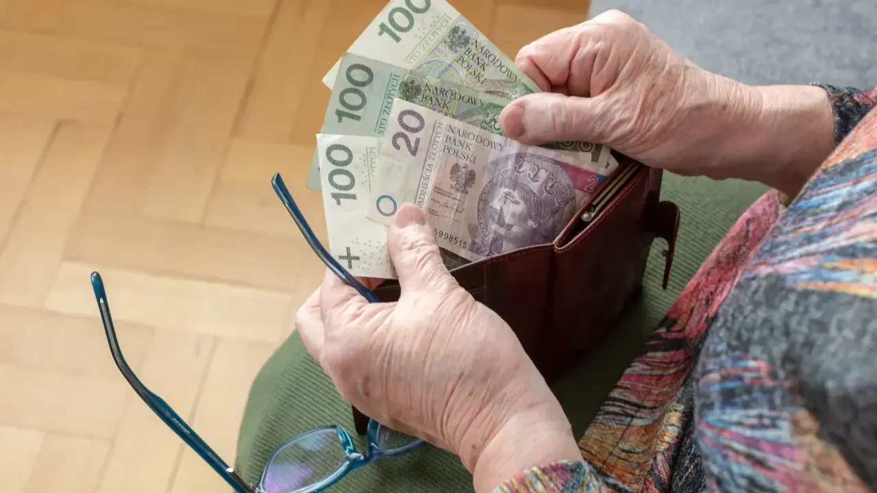 Dłonie starszej osoby wyciągają pieniądze z portfela. Widać banknoty 100 zł i 20 zł, być może to oczekiwana trzynasta emerytura.