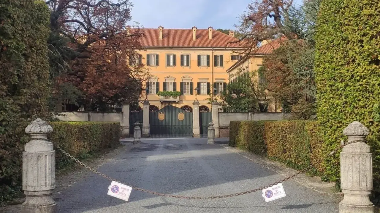 Ingresso di Villa San Martino ad Arcore, con cancello verde e alberi autunnali. Catena con cartelli di divieto di sosta blocca l'accesso.