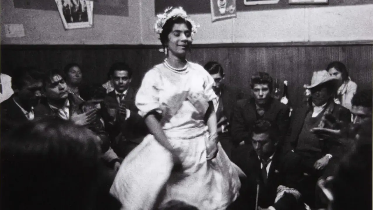 Una mujer con corona de flores baila en una celebración, rodeada de gente. Podría ser una boda gitana.