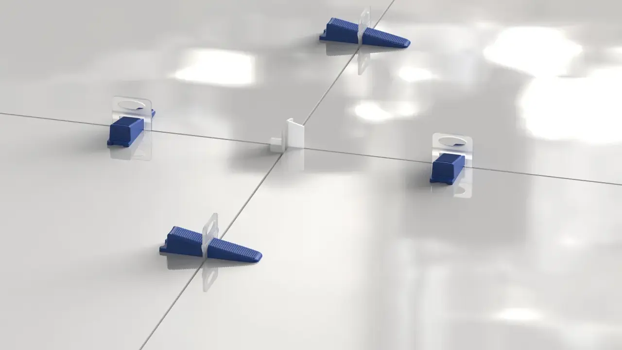 Sistema de nivelación de baldosas con cuñas azules y separadores blancos. La **matajunta desplazada** asegura una instalación perfecta.