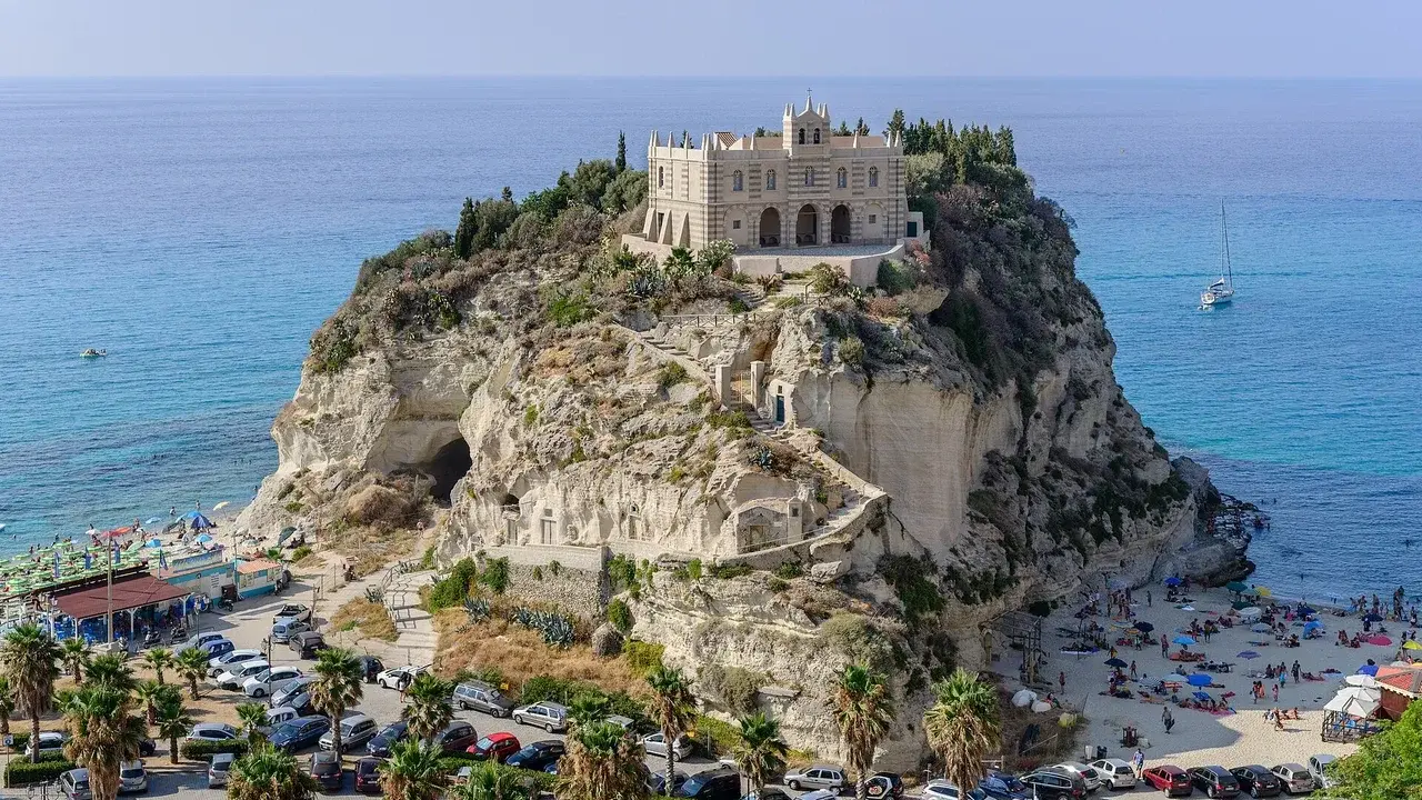 Santuario di Santa Maria dell'Isola a Tropea, regione Calabria, su uno sperone roccioso a picco sul mare azzurro, con spiaggia e palme.