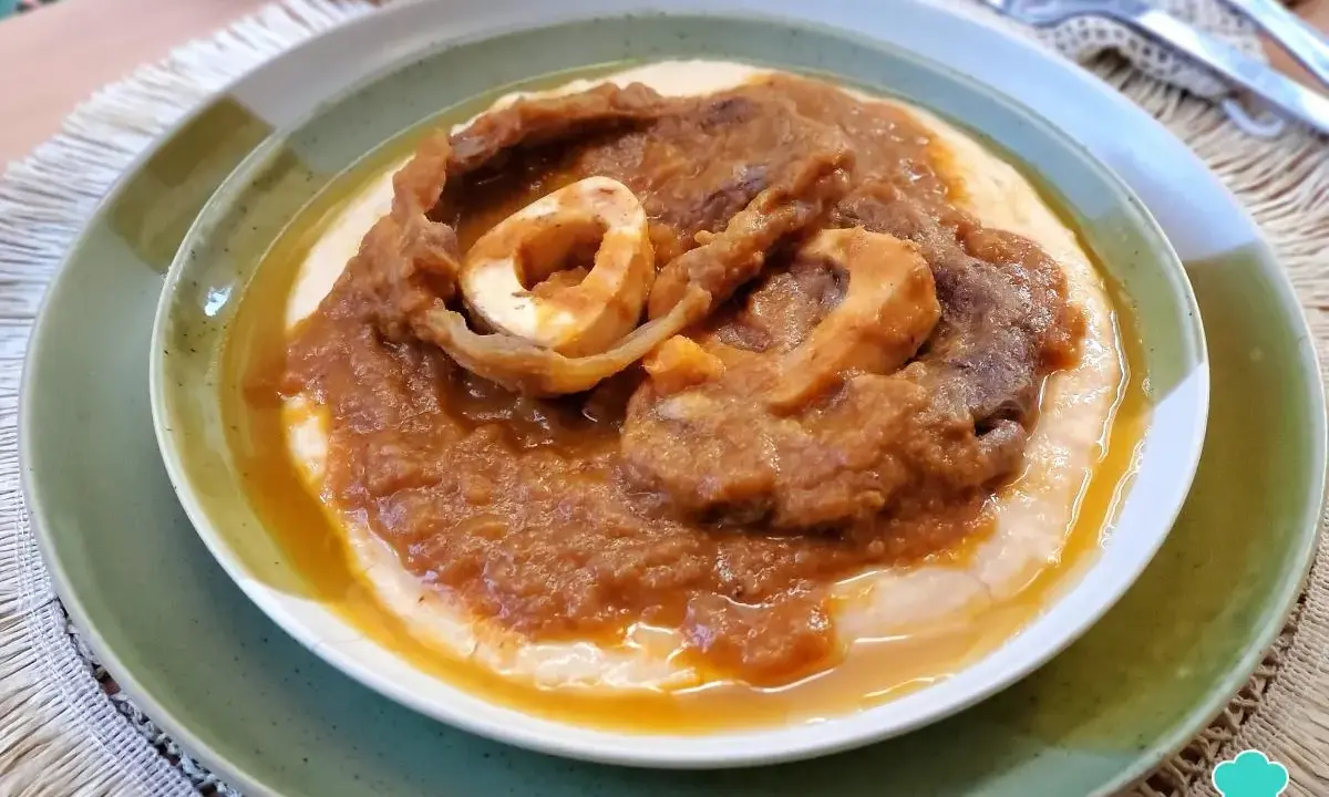 Un plato de osobuco de ternera cocinado a fuego lento, servido sobre una cama cremosa de polenta.